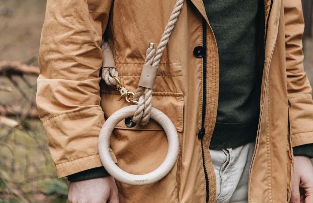 Close-up of hemp dog leash with polished dead Ash wood round handle, draped across man's body and attached with carabiner to O-ring near handle.