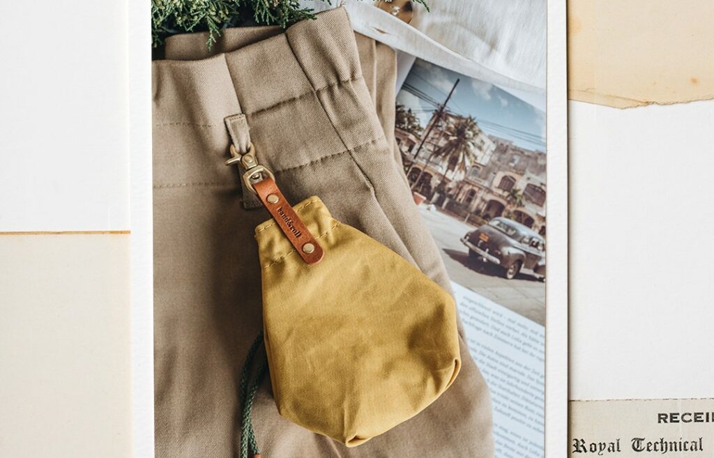 Mustard waste bag dispenser with Italian vegetable-tanned leather fittings, made of water-repellent waxed cotton canvas, attached to a pair of pants.
